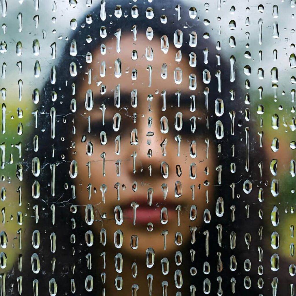 Raindrops form binary on shattered glass, warped face.